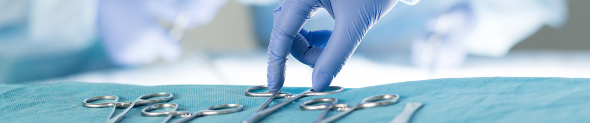 Dłoń w rękawiczce sięga po instrumentarium neurochirurgiczne wyłożone na stole, wybiera jedne z czterech nożyczek.